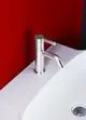 Chromventil von Ideal Standard mit schlichter Ausführung, montiert auf einer weißen Waschtischoberfläche, vor roter Wand. Wasserabfluss durch kreisförmigen Ablauf.